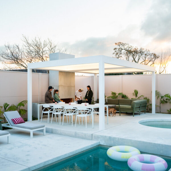 Poolside pergola at dusk with an outdoor fireplace and seating, pool floats in the water