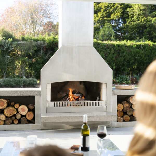 Family seated at an outdoor dining table in the evening, gathered in front of a lit outdoor fireplace