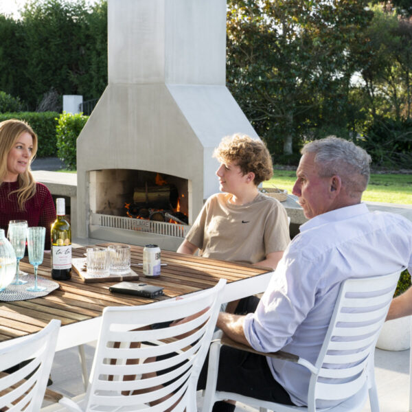 Wine poured beside a lit outdoor fireplace, with firewood stacked in the base and a clipped hedge behind