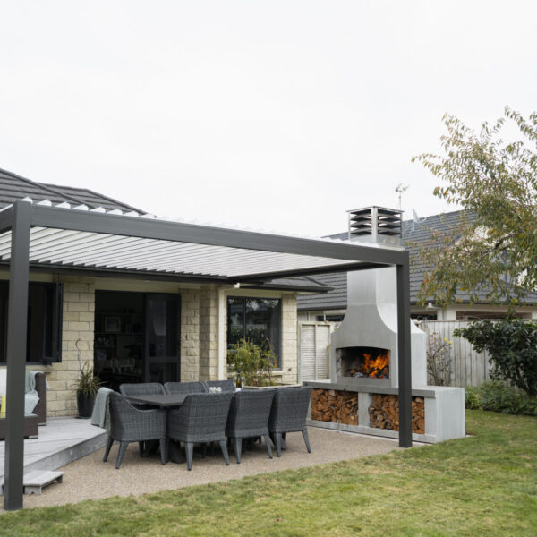 White outdoor fireplace under a louvred roof, positioned well clear of the boundary fence