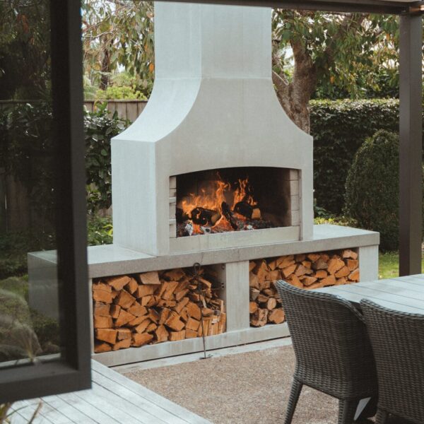 White outdoor fireplace with firewood stored beneath it and lounge seating pulled in close
