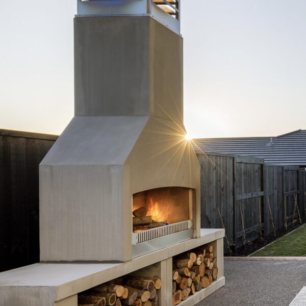 Concrete outdoor fireplace lit at sunset, with the last of the sun flaring behind the chimney