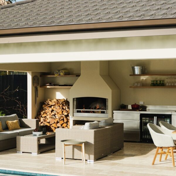 Outdoor fireplace built into a run of kitchen cabinetry, with firewood stacked alongside