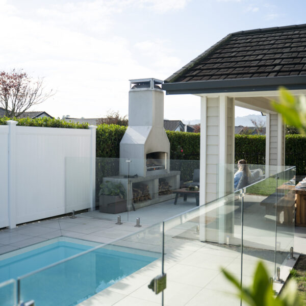Outdoor fireplace sized to a compact poolside courtyard, with glass pool fencing alongside