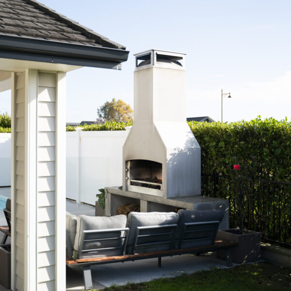 Outdoor fireplace set close to the house with a clipped hedge along the boundary behind
