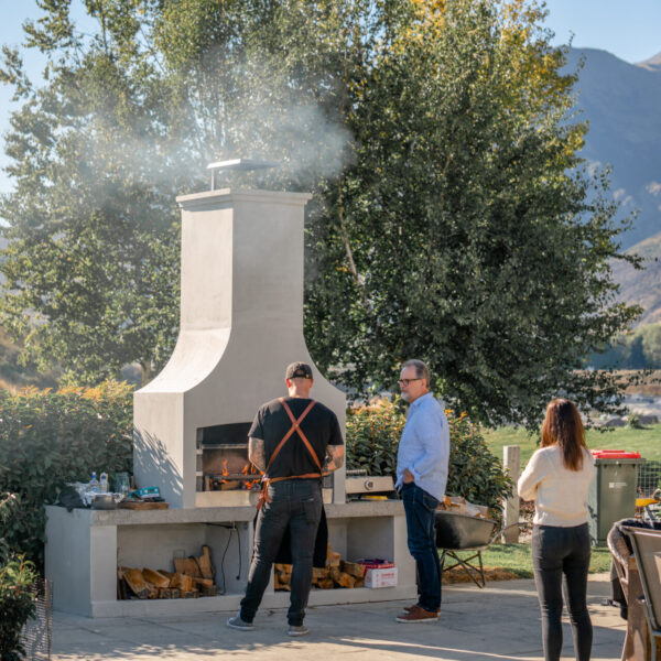 Plastered white outdoor fireplace with people gathered around it, mountains in the distance