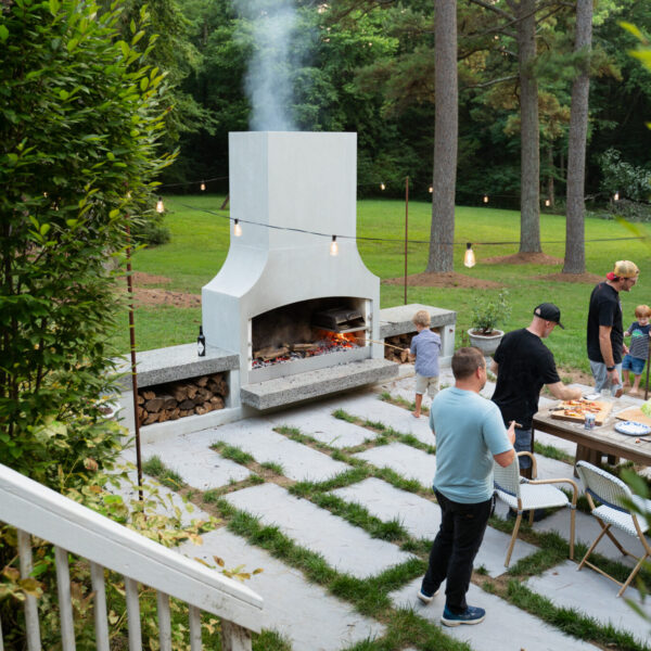 Tall white outdoor fireplace anchoring a large lawn area with seating and tables around it